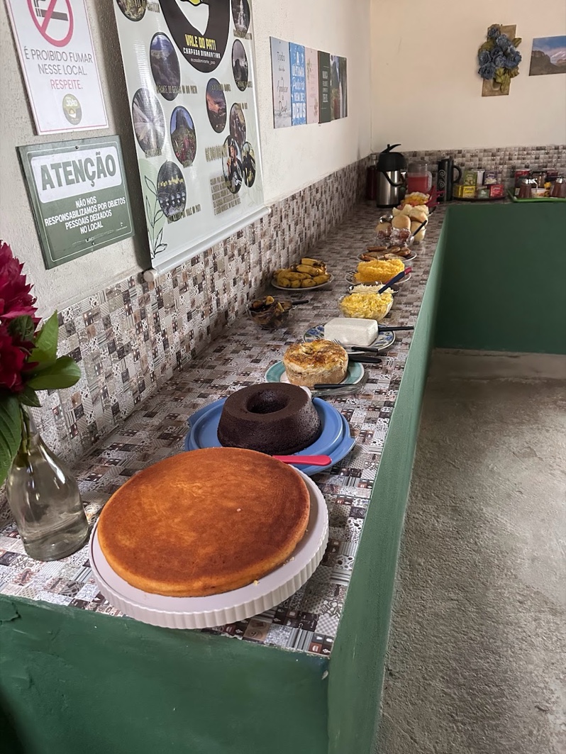 Mesa de café da manhã farta numa casa dos Patiseiros — bolos, cuscuz, ovos, frutas e café